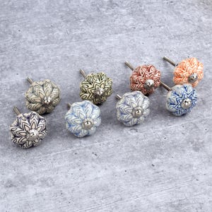 May include: Eight ceramic cabinet knobs with floral patterns in shades of blue, green, and orange. The knobs have a silver metal base.