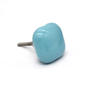 May include: A light blue ceramic cabinet knob with a square shape and a silver screw.