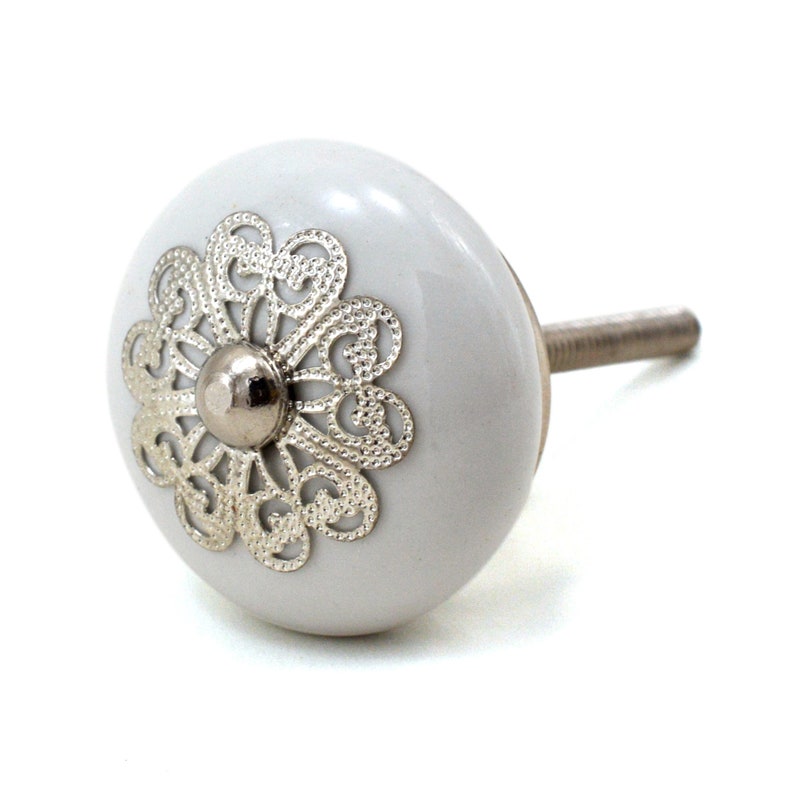 White ceramic cabinet knob with a silver flower motif and gold center; decorative furniture knob for cabinets and drawers.