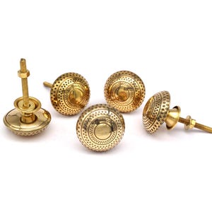 Puede incluir: Cuatro pomos de armario dorados con un diseño circular y un centro elevado. Los pomos tienen una superficie texturizada con pequeños puntos.