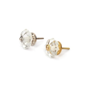 May include: Two clear glass cabinet knobs with a faceted, flower-like shape. One knob features a silver-toned metal base and center cap, while the other knob has a gold-toned metal base and center cap, both with threaded metal mounting screws.