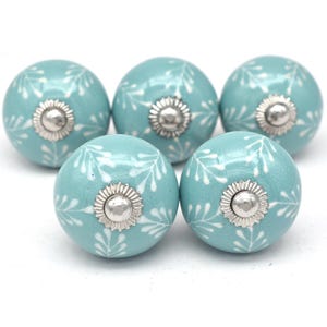 May include: Five aqua blue ceramic cabinet knobs with a white floral design and silver accents.