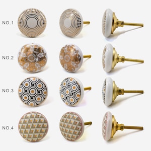 May include: Four sets of ceramic cabinet knobs with different geometric patterns. Each set includes a knob with a gold screw and a matching knob without a screw. The patterns include a gold and white dot pattern, a gold and white floral pattern, a black and white geometric pattern, and a pink and gold geometric pattern.