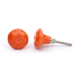 May include: A collection of twelve decorative cabinet knobs in various colours and patterns. Each knob features a round or oval shape with a metal bolt extending from the back. The designs include floral, geometric, and solid textures in shades of green, blue, orange, purple, white, and grey.