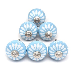 Six sky-blue ceramic cabinet knobs with white daisy patterns and silver centers, perfect as drawer knobs for cabinets.