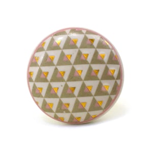 Pode incluir: Um botão redondo de cerâmica com um padrão geométrico de triângulos rosa e dourados sobre um fundo branco.