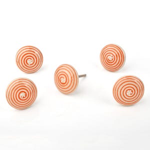 Pode incluir: Cinco puxadores de armário de cerâmica creme com um design de espiral laranja concêntrico. Cada puxador tem um pequeno centro branco sujo e uma haste de metal. Adequado para projetos de móveis ou decoração de casa.