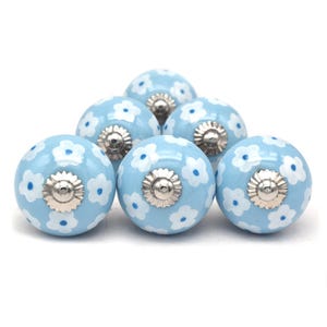 Group of hand-painted sky-blue ceramic cabinet knobs featuring white floral pattern and silver mounting hardware.
