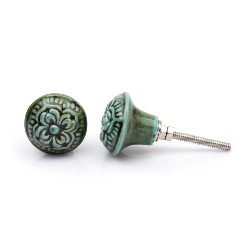 May include: A collection of twelve decorative cabinet knobs in various colours and patterns. Each knob features a round or oval shape with a metal bolt extending from the back. The designs include floral, geometric, and solid textures in shades of green, blue, orange, purple, white, and grey.