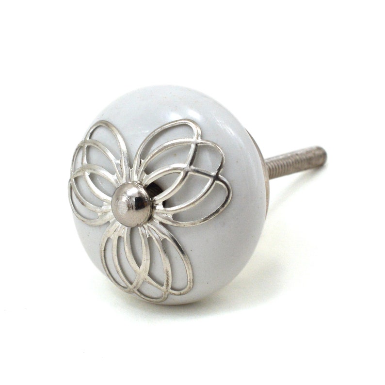 White ceramic cabinet knob with a silver flower motif and gold center; decorative furniture knob for cabinets and drawers.