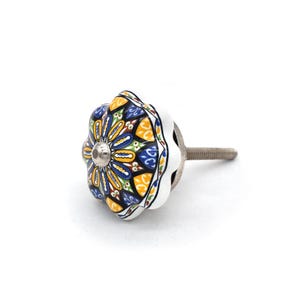 May include: A decorative ceramic cabinet knob with a floral design. The knob features a white base with a colorful pattern of blue, yellow, and green. A silver-colored screw extends from the back for installation.