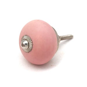 May include: A pink ceramic cabinet knob with a silver metal base and screw. The knob has a round shape with a silver decorative accent in the center. The screw extends approximately 1.5 inches.