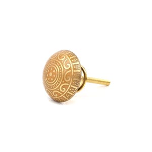 May include: A decorative brass cabinet knob with an intricate, embossed circular design. The knob features a detailed pattern of swirls and dots, and a threaded post for easy installation. The knob is a warm, golden colour.