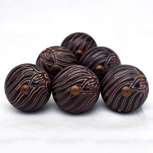 Könnte beinhalten: Sechs braune Holzgriffe mit einem weißen Wirbelmuster und einem Messingakzent. Die Griffe sind in Pyramidenform angeordnet.