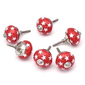 Może przedstawiać: Sześć czerwonych ceramicznych gałek do szafek z białymi gwiazdkami. Każda gałka ma srebrną śrubę.