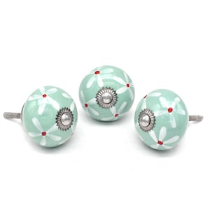 May include: Three ceramic knobs with a light green background and white flowers with red centres. The knobs have a silver metal base.
