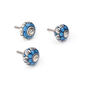 Assorted hand-painted ceramic knobs in blue, black and white with mandala and floral motifs for cupboard handles and kitchen decor.
