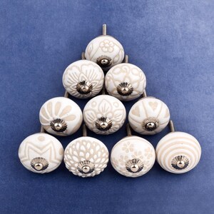 collection of white ceramic drawer knobs with intricate floral patterns and silver accents. The knobs are arranged in a basket lined with peach-colored fabric.