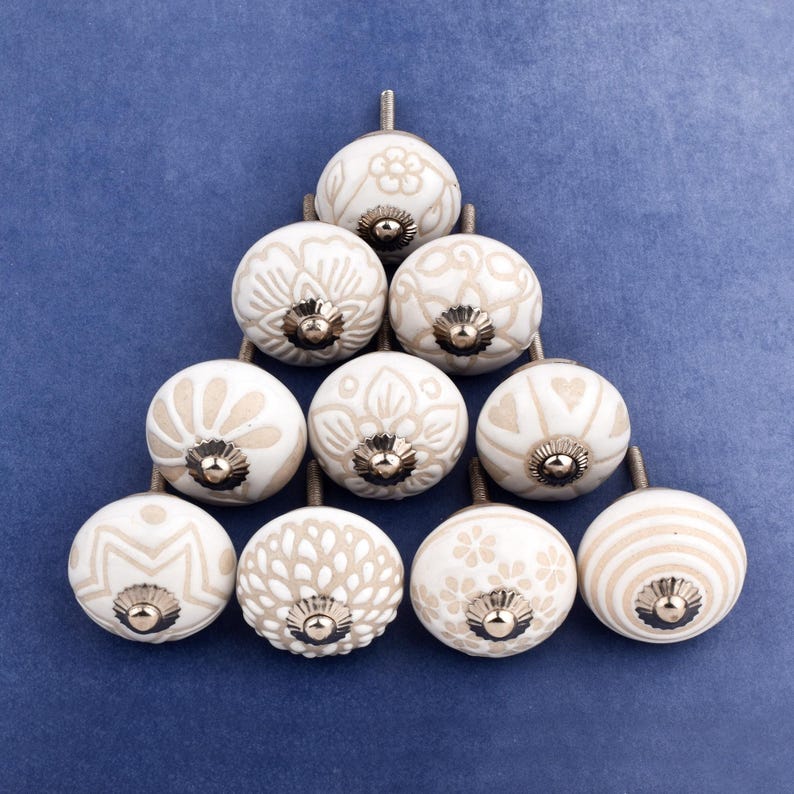 collection of white ceramic drawer knobs with intricate floral patterns and silver accents. The knobs are arranged in a basket lined with peach-colored fabric.