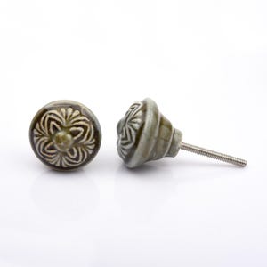 May include: A collection of twelve decorative cabinet knobs in various colours and patterns. Each knob features a round or oval shape with a metal bolt extending from the back. The designs include floral, geometric, and solid textures in shades of green, blue, orange, purple, white, and grey.