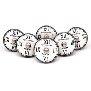 Peut inclure: Six boutons en céramique blanche avec des cadrans d'horloge romains noirs et des accents argentés. Chaque bouton porte le texte "POTTER-STONE" et un motif floral décoratif.