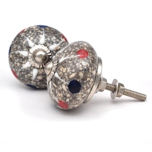Peut inclure: Deux boutons de cabinet en céramique avec une finition gris mouchetée. Un bouton a des accents blancs et bleus, tandis que l'autre a des accents rouges et bleus. Les deux boutons ont une vis en métal argenté.