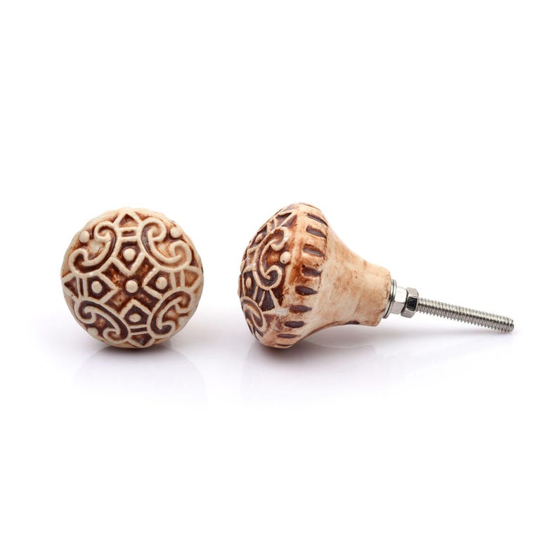 May include: A collection of twelve decorative cabinet knobs in various colours and patterns. Each knob features a round or oval shape with a metal bolt extending from the back. The designs include floral, geometric, and solid textures in shades of green, blue, orange, purple, white, and grey.