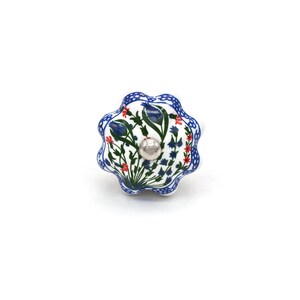 May include: A decorative ceramic cabinet knob with a floral design. The knob features a white base with blue, red, and green floral patterns. The edges are outlined in blue, and the center has a silver-colored metal screw.