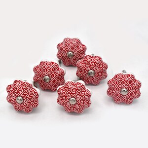Op de afbeelding: Zes rood-wit patroon keramische kastknoppen met zilverkleurige hardware. De knoppen hebben een bloemvorm met een herhalend wervelontwerp. De knoppen zijn gerangschikt op een witte achtergrond.