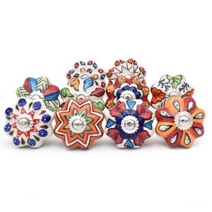 Könnte beinhalten: Zehn bunte Keramik-Schubladengriffe mit Sternmuster. Jeder Griff hat ein anderes Muster in Rot, Orange, Gelb, Blau, Grün und Weiß.