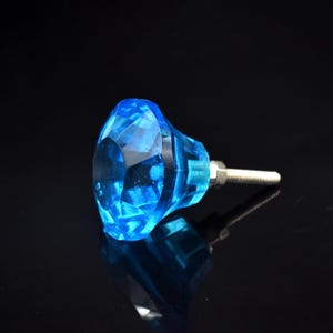 May include: A faceted, blue crystal cabinet knob with a silver screw. The knob is a vibrant, transparent blue and reflects light. The hardware is designed for furniture and home decor.