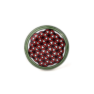 May include: A circular cabinet knob featuring a red and black floral design on a white background. The knob has a green and black border. Suitable for drawers and cabinets.