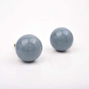 May include: Two spherical cabinet knobs with a smooth, glossy, slate blue finish. Each knob features a rounded, ball-shaped head and a small metallic attachment point visible at the base, designed for mounting onto furniture or cabinetry doors.