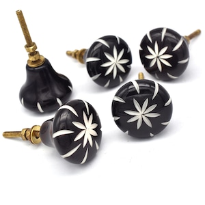May include: Five black ceramic cabinet knobs with a white floral design. Each knob has a brass screw.