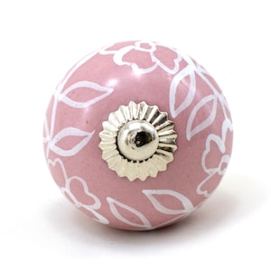 May include: A pink ceramic knob with a white floral design. The knob has a silver metal base.
