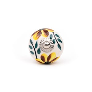 Peut inclure: Un bouton de meuble rond en céramique à base blanche orné de motifs de tournesols peints à la main en jaune et marron avec des feuilles vertes. Le centre du bouton présente un capuchon cannelé en métal argenté avec une petite vis au milieu.