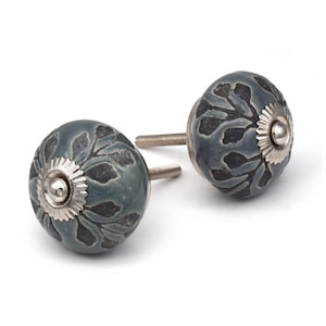May include: Two gray ceramic cabinet knobs with a black floral design. The knobs have a silver metal screw and a silver metal base.
