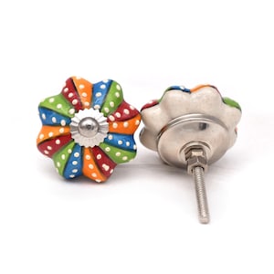 Könnte beinhalten: Zwei blütenförmige Schrankknöpfe in leuchtenden Farben. Die Knöpfe weisen ein Regenbogenmuster mit roten, orangefarbenen, grünen und blauen Segmenten auf, die mit weißen Tupfen verziert sind. Die Hardware ist silberfarben.