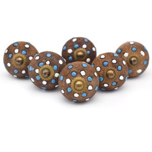Op de afbeelding: Zes bruine keramische knoppen met witte en blauwe stippen. Elke knop heeft een gouden midden.