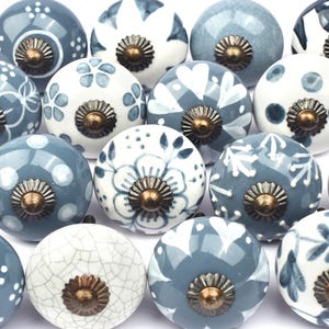 Könnte beinhalten: Sortiment von 15 Keramik-Schrankknöpfen mit einem blauen und weißen Blumenmuster. Die Knöpfe haben eine Messing-Oberfläche und sind perfekt, um jedem Raum einen Hauch von Landhausstil zu verleihen.