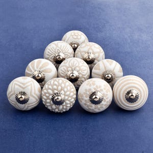 collection of white ceramic drawer knobs with intricate floral patterns and silver accents. The knobs are arranged in a basket lined with peach-colored fabric.