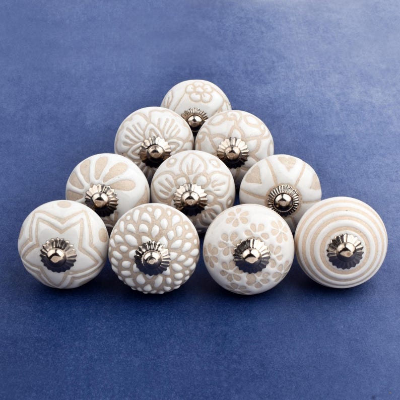 collection of white ceramic drawer knobs with intricate floral patterns and silver accents. The knobs are arranged in a basket lined with peach-colored fabric.