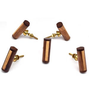 Puede incluir: Cinco pomos de madera para armario con base de latón. Los pomos están hechos de dos tipos diferentes de madera, creando un patrón a rayas.