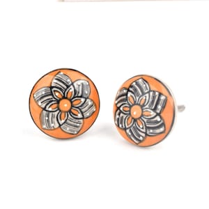 May include: Two orange ceramic cabinet knobs with a floral design. The flower has black and white striped petals and a small orange centre. The knobs have a silver metal screw for installation.