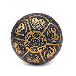 Etched brass flower cabinet knob with ornate gold pattern on dark background; decorative cabinet knobs for dresser hardware.