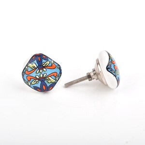 May include: Two decorative cabinet knobs with a white base and a colorful floral design. The knobs feature a square shape with a blue background, orange and green floral patterns, and a silver metal screw.