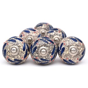 Può includere: Set di sei pomelli per armadi in ceramica con sfondo beige maculato, motivo a foglie blu e dettagli rossi. I pomelli hanno una base in metallo argentato.