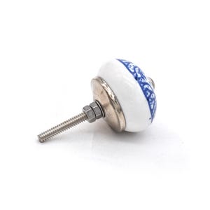Pode incluir: Puxador de arm&aacute;rio de cer&acirc;mica branca e azul com um design floral. O puxador tem uma base de metal prateado e um parafuso roscado para instala&ccedil;&atilde;o. Um detalhe decorativo para m&oacute;veis.