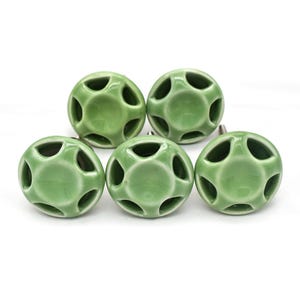 Könnte beinhalten: Fünf grüne Keramik-Schrankknöpfe mit einem fünfzackigen Sternmuster. Jeder Knopf hat eine silberne Schraube.