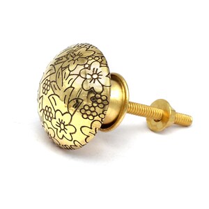 Puede incluir: Pomo de armario dorado con un diseño floral. El pomo tiene una base de tornillo.